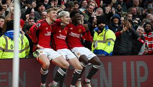 Tiga pemain Manchester United, Rasmus Hojlund, Alejandro Garnacho, dan Kobbie Mainoo duduk di atas papan iklan lapangan Old Trafford sebagai bentuk selebrasi gol yang dicetak ke gawang West Ham United dalam laga pekan ke-23 Premier League 2023/2024, Minggu (4/2/2024) malam WIB. (Paul ELLIS / AFP)