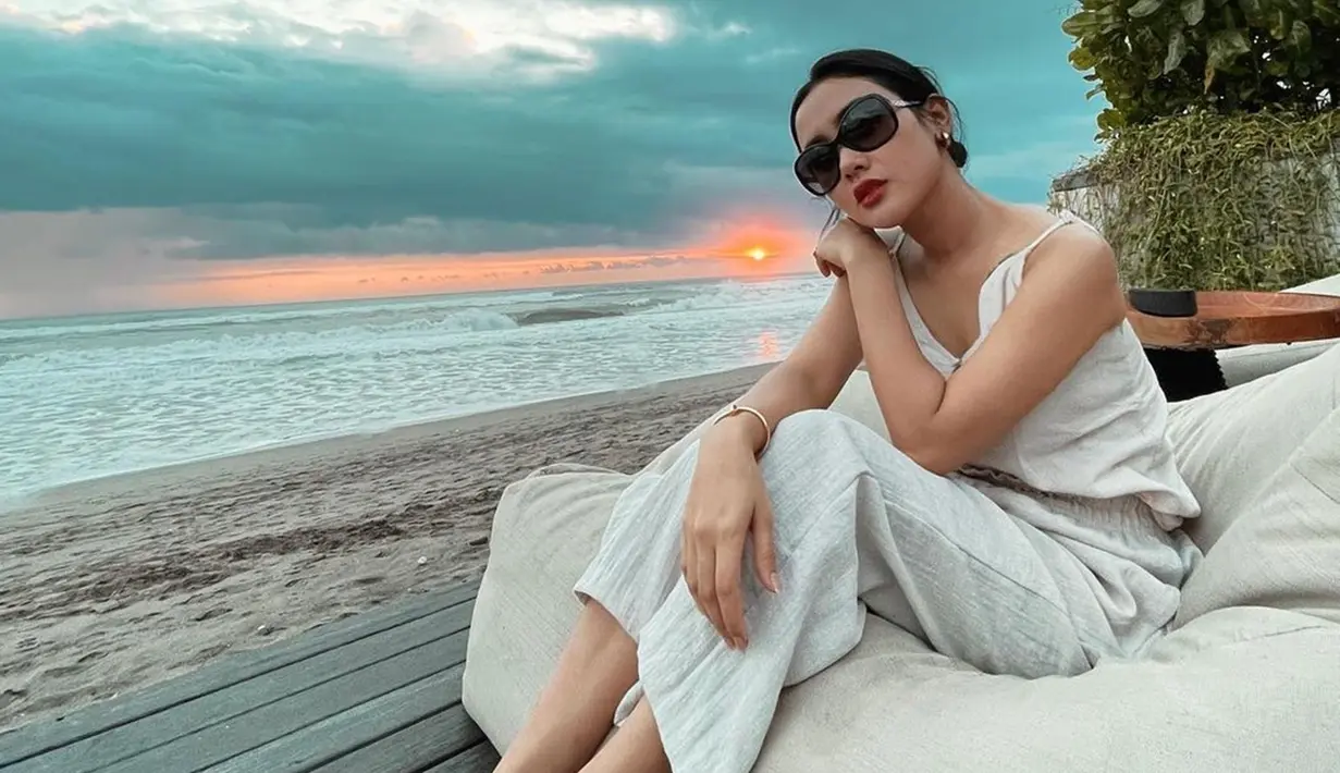 Cita Citata pancarkan pesona saat berfoto dengan latar belakang air laut kala sunset. Dengan outfit putih tulang dan tambahan aksesoris kacamata, ia seperti mutiara yang tersembunyi di laut. Angin sepoi juga meniupkan setiap helai rambutnya. (Liputan6.com/IG/@cita_citata)