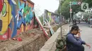 Seorang pria duduk di dekat tembok Jalan Juanda yang ambruk di kawasan Depok, Jawa Barat, Senin (2/12/2019). Kondisi tembok yang dipenuhi mural tersebut mulai rapuh dan sebagian sisinya telah ambruk serta miring sehingga membahayakan pejalan kaki. (Liputan6.com/Immanuel Antonius)