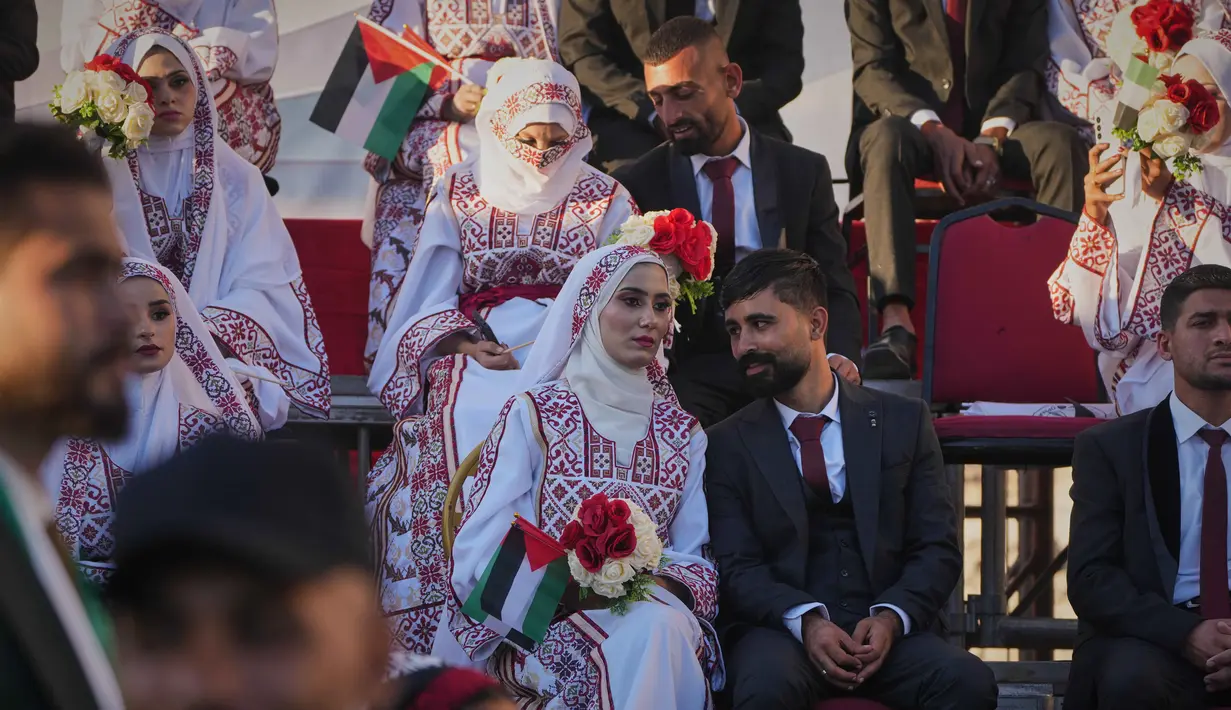 Suara gendang yang menggema dan sambutan meriah dari para keluarga serta warga sekitar menghidupkan kembali suasana yang selama ini dipenuhi kesedihan. Tampak dalam foto, pasangan Palestina Hikmat Lawwa dan Eman Lawwa, tengah, bergabung dengan pasangan pengantin baru lainnya dalam upacara pernikahan massal di Kota Hamad, Khan Younis, Jalur Gaza, Selasa 2 Desember 2025. (AP Photo/Abdel Kareem Hana)