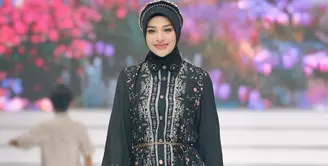 Aurel Hermansyah tampil dengan brand Shi by Shireen Sungkar. Ia mengenakan atasan kemeja hitam bercorak bunga lengan panjang pump dipadukan kerudung warna senada serta bondu beads. Ia memilih skirt panjang baby blue dengan aksen bulu-bulu. [@aurelie.hermansyah]