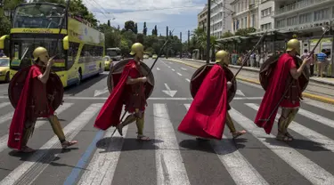 Sekelompok Pria berpakaian seperti tentara Yunani kuno menyeberang jalan sambil membawa tombak, perisai saat pertunjukan di Konstitusi (Syntagma) persegi di Athena, Yunani (21/6/2015). (REUTERS /Marko Djurica)