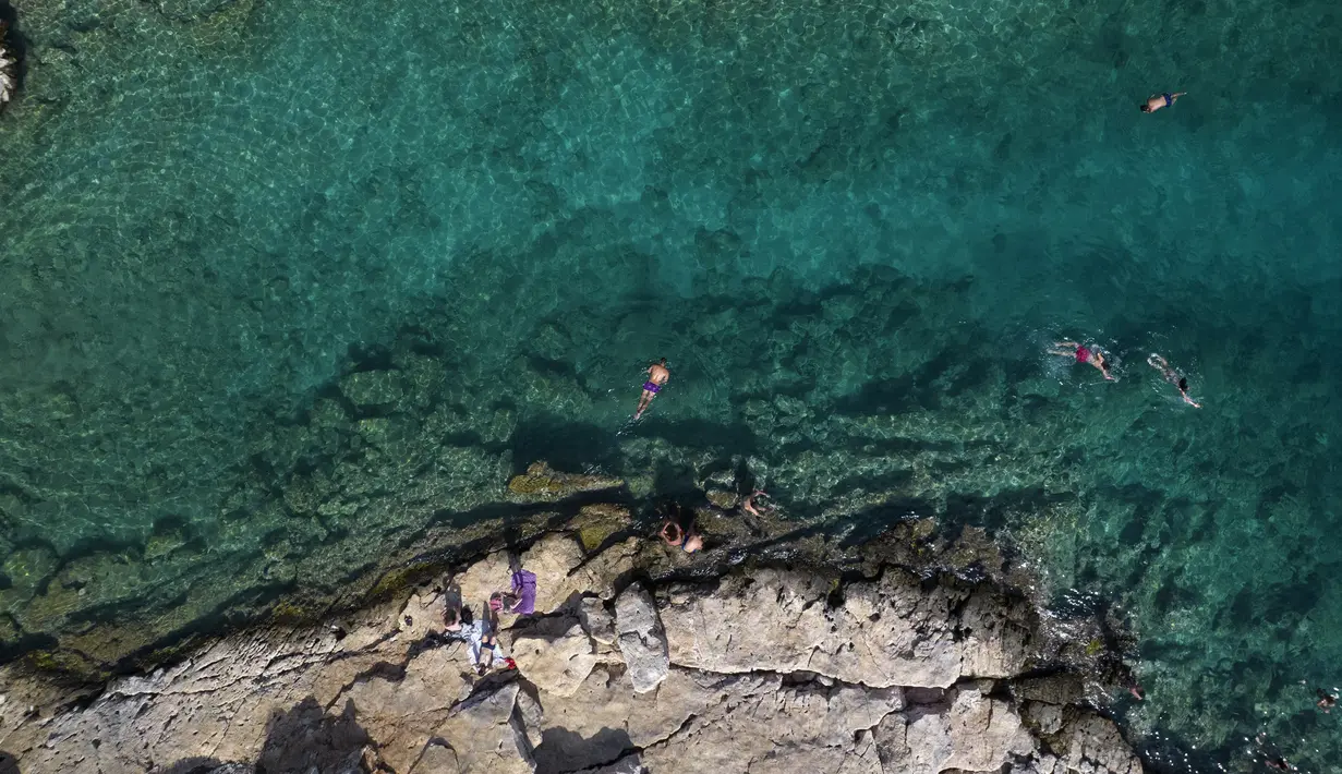 Orang-orang berenang di laut di pinggiran Vouliagmeni, barat daya Athena, Yunani, Kamis (29/7/2021). Gelombang panas membuat orang-orang berbondong-bondong ke pantai, air mancur umum, dan lokasi ber-AC. (AP Photo/Yorgos Karahalis)