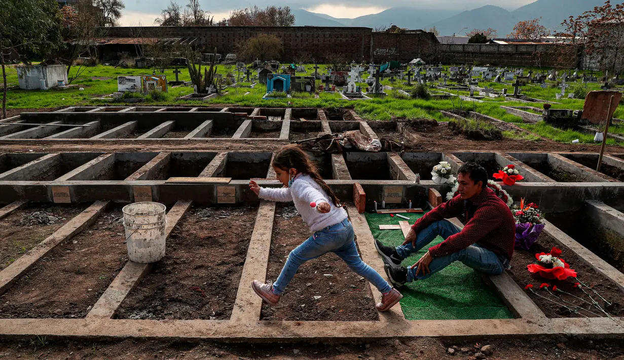 Jose Collantes dan sang putri, Kehity (5) mengunjungi makam istrinya Silvia Cano yang meninggal karena COVID-19 sebulan lalu di Pemakaman Katolik di Santiago, Chili, 5 Agustus 2020. Mereka yang selamat dari pandemi dan yang kehilangan orang yang dicintai, tragedi itu tetap ada. (AP/Esteban Felix)