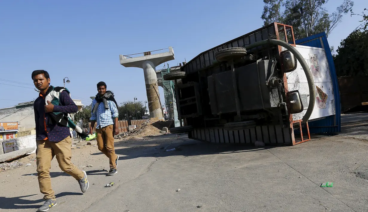 Warga berjalan di dekat kendaran yang terbalik akibat demonstrasi di negara bagian Haryana, India,Minggu (21/2). Pihak berwenang mengambil langkah mengatasi masalah pasokan air yang menimbulkan aksi kekerasan yang menewaskan 10 orang (REUTERS/Adnan Abidi)