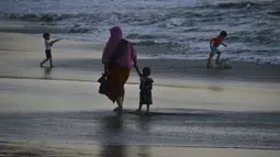 Seorang wanita bersama putranya berjalan di tepi pantai saat matahari terbenam di Banda Aceh pada 28 Juni 2019. Suasana eksotis menuju temaram bisa dinikmati sembari berjalan menyusuri pantai di tengah cahaya matahari yang mulai memerah. (Photo by CHAIDEER MAHYUDDIN / AFP)