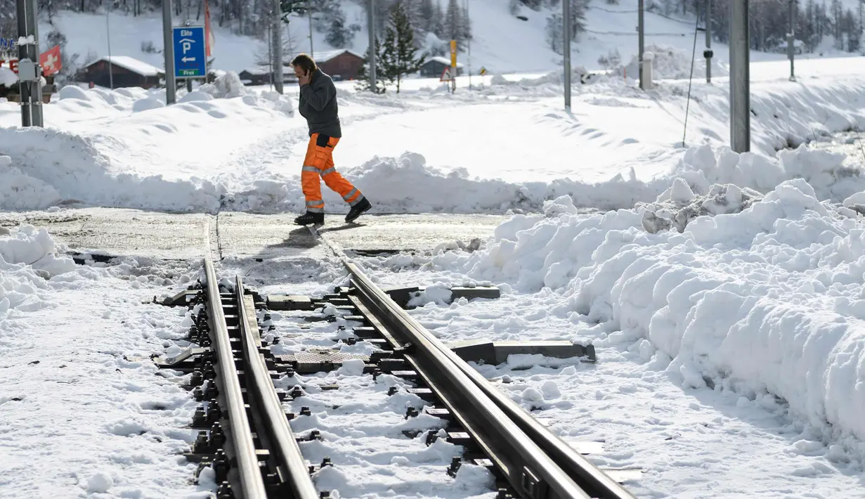 Seorang petugas memeriksa kondisi rel kereta api yang tertutup salju tebal di salah satu resor ski paling populer di Swiss (10/1). Sekitar 13.000 wisatawan terjebak akibat bencana tersebut. (AFP Photo/Fabrice Coffrini)