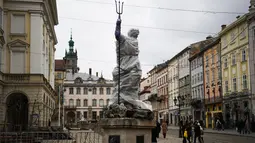 Pejalan kaki berjalan melewati patung yang dibungkus dengan plastik pelindung di sebelah Katedral Latin di Lviv, 5 Maret 2022. Warga kota Lviv membungkus semua patung untuk melindungi warisan sejarahnya dari kerusakan akibat serangan di tengah konflik Rusia-Ukraina. (Daniel LEAL/AFP)