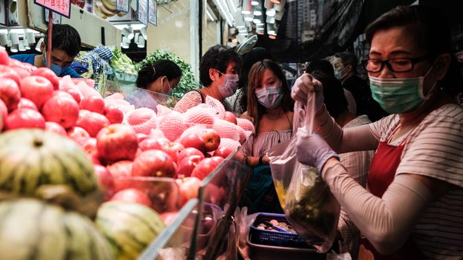 Pedagang mengenakan masker melayani pelanggan di toko buah dan sayuran di Hong Kong (21/4/2020). Hong Kong melaporkan penurunan kasus infeksi harian Covid-19, tetapi pemerintah kota mengatakan mereka tidak mengambil risiko apa pun. (AFP/Anthony Wallace)