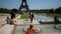 Sejumlah warga Paris memilih mengademkan diri di air mancur di halaman Menara Eiffel karena gelombang panas yang melanda Eropa pada Selasa, 1 Juli 2025. (dok. Dimitar DILKOFF / AFP)