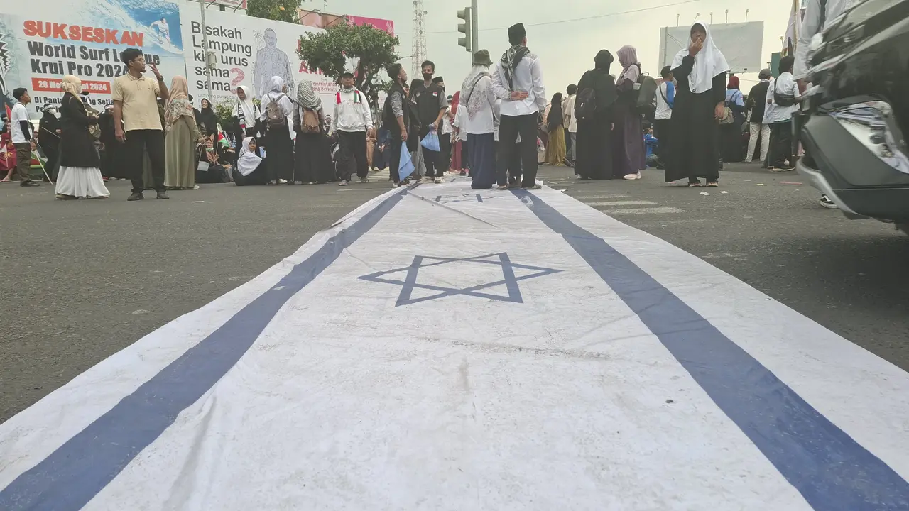 Massa aksi solidaritas kemanusiaan Lampung bersama Palestina jilid II menginjak bendera Israel saat unjuk rasa di Tugu Adipura, Bandar Lampung.  Foto : (Liputan6.com/Ardi).