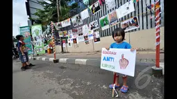 Seorang anak kecil tampak berdiri di depan pameran meme tentang korupsi yang digelar di Jalan MH Thamrin, Jakarta, Minggu (18/1/2015). (Liputan6.com/Miftahul Hayat)