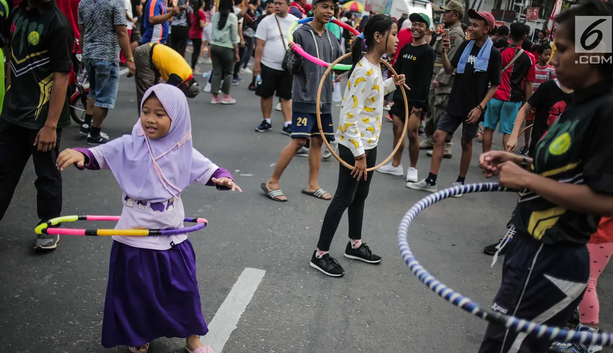 Anak-anak bermain permainan tradisional hula hoop ditemani sejumlah mahasiswa dari Penggerak Olahraga saat car free day (CFD) di kawasan Bundaran HI, Jakarta, Minggu (14/7/2019). Kegiatan yang rutin digelar ini bertujuan mengajak masyarakat DKI Jakarta aktif berolahraga. (Liputan6.com/Faizal Fanani)