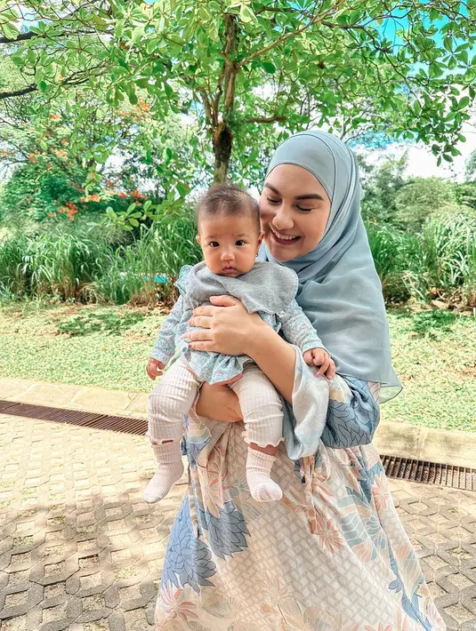 Kembali berpose dengan anak keduanya, outfit Irish Bella dan sang buah hati kompak berwarna biru muda. Irish tampil cantik dengan gamis bermotif floral, dipadu hijab lebar yang serasi. Sedangkan putrinya tampak mengenakan atasan bermotif bunga-bunga kecil, celana panjang dan kaus kaki putih, serta slaber bayi abu-abu. Foto: Instagram.