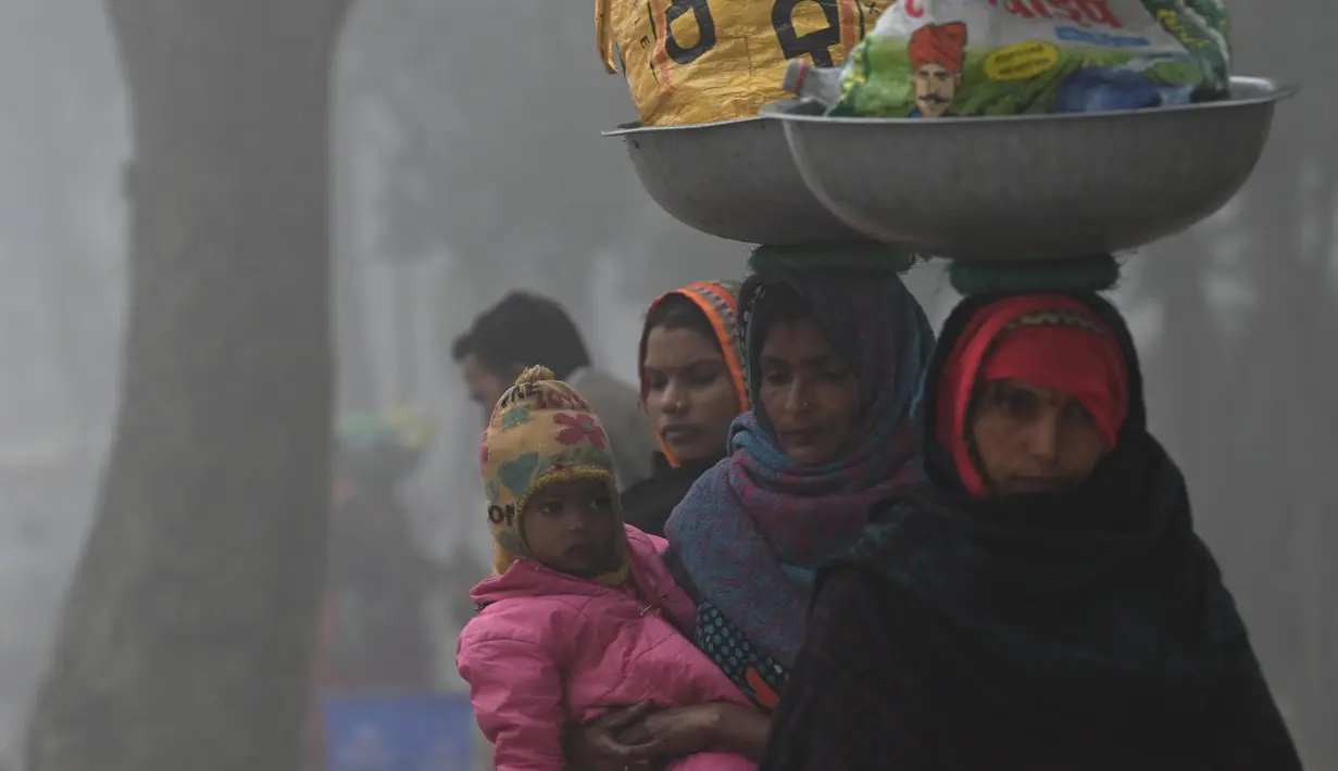 Seorang pekerja yang menggendong anaknya berjalan di sepanjang jalan di dekat Gerbang India di tengah kabut asap tebal di New Delhi pada 22 Februari 2023. (Arun SANKAR/AFP)