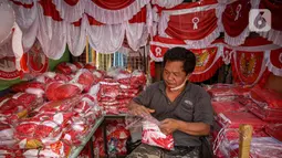 Pedagang merapikan pernak pernik HUT Republik Indonesia di Pasar Jatinegara, Jakarta, Selasa (10/8/2021). Dua tahun pandemi Covid-19 berjalan, penjual pernak pernik hingga bendera merah putih  turun 50-70 persen serta daya beli masyarakat pun turun karena PPKM Darurat. (Liputan6.com/Faizal Fanani)