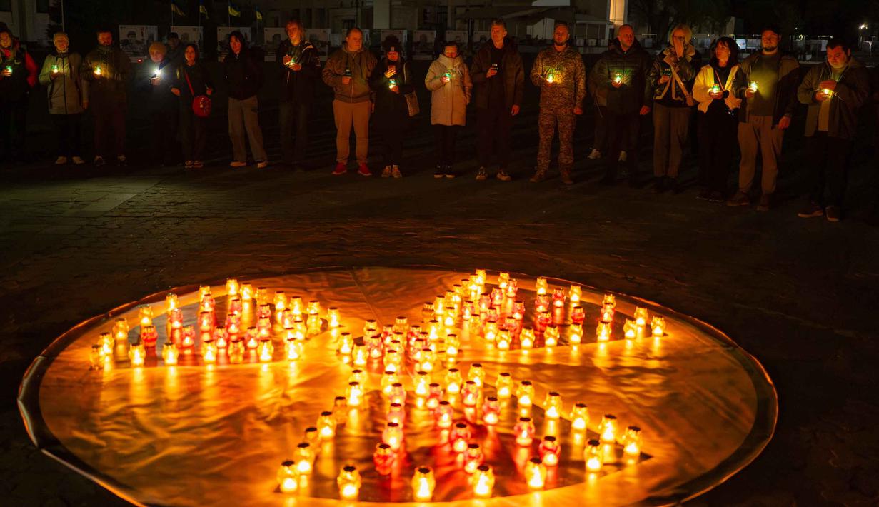 Orang-orang memegang lilin di depan simbol bahaya radiasi di sebuah monumen yang didedikasikan untuk petugas pemadam kebakaran dan pekerja yang meninggal setelah bencana nuklir Chernobyl, menjelang peringatan 40 tahunnya di Slavutych, Ukraina, Sabtu, 25 April 2026. (AP Photo/Dan Bashakov)