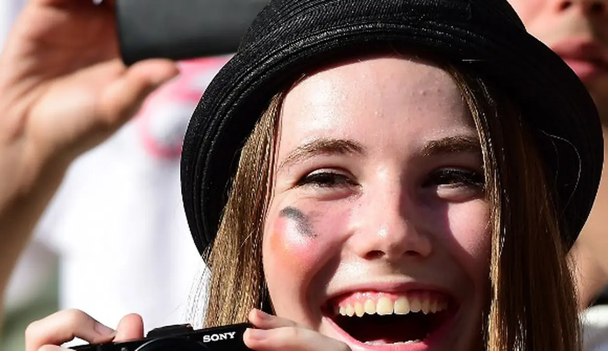 Sambil memegang kamera seorang suporter cantik tersenyum sebelum Jerman berlaga melawan Ghana di The Castelao Stadium, Fortaleza (21/06/2014) (AFP PHOTO/JAVIER SORIANO)
