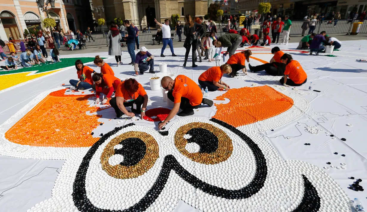 Sejumlah relawan membuat mosaik raksasa dari 100 ton limbah tutup botol di kota Novi Sad, Serbia, Sabtu (30/9). Hampir 800.000 tutup botol dibutuhkan dalam proyek meningkatkan bantuan bagi anak-anak penyandang cacat tersebut. (AP/Darko Vojinovic)