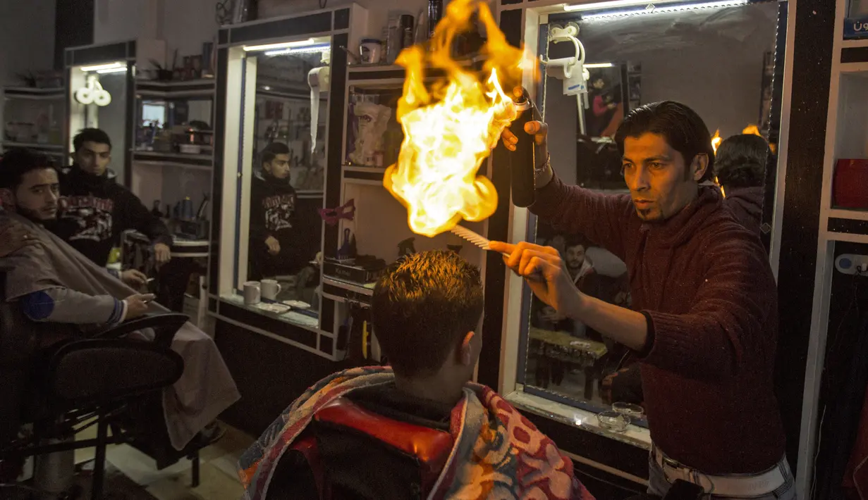Ramadan Edwan, seorang tukang cukur asal Palestina, menggunakan api untuk mencukur rambut pelanggannya di sebuah barbershop di kamp pengungsian Rafah, di selatan Jalur Gaza, Rabu (1/2). (MAHMUD HAMS/AFP)