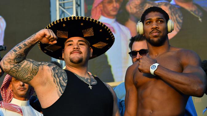 Petinju kelas berat Anthony Joshua (kanan) dan Andy Ruiz Jr (kiri) berpose saat timbang badan resmi di Riyadh, Arab Saudi, Jumat (6/12/2019). Pertandingan kedua antara Anthony Joshua dengan Andy Ruiz Jr dijuluki sebagai 'Clash on the Dunes'. (Giuseppe CACACE/AFP)