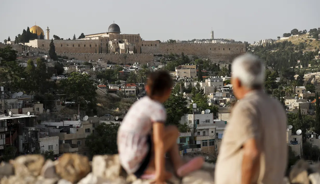 Seorang pria dan anak-anak Palestina melihat ke Masjid Kubah Batu (kiri) dan masjid Al-Aqsa (kanan), di halaman tertutup masjid Al-Aqsa, selama bulan suci Ramadan, ketika mereka menunggu panggilan untuk salat selama krisis pandemi coronavi di Kota Tua Yerusalem (19/5/2020). (AFP/Ahmad Gharabli)
