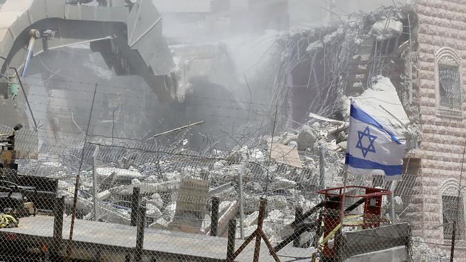 Bendera Israel terlihat selama penghancuran bangunan Palestina di daerah Wadi al-Hummus yang berdekatan dengan Palestina (22/7/2019). Palestina menuduh Israel menggunakan keamanan sebagai dalih untuk mengusir mereka dari Tepi Barat. (AFP Photo/Ahmad Gharabli)