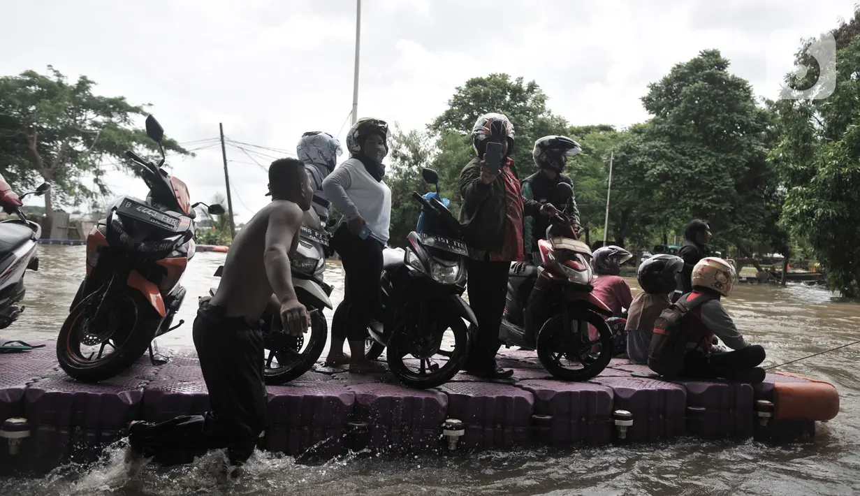 Pengendara sepeda motor menggunakan jasa rakit saat banjir melanda Cempaka Putih, Jakarta, Minggu (23/2/2020). Pengendara memanfaatkan jasa angkutan rakit yang ditawarkan warga agar dapat melewati banjir. (merdeka.com/Iqbal S. Nugroho)