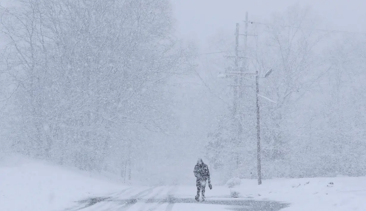 Seorang pria berjalan di bawah salju lebat saat terjadi badai salju di Manville, New Jersey (21/3). Salju tebal yang menutup jalanan ini berpotensi membahayakan warganya. (AP/Julio Cortez)