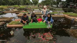 Genangan air yang menutupi area pemakaman membuat akses jalan antar-blok makam menjadi terbatas. Peziarah harus ekstra hati-hati melewati lumpur dan air yang masih menggenang. Tampak dalam foto, warga mengunjungi makam anggota keluarga mereka di Tempat Pemakaman Umum (TPU) Semper, Cilincing, Jakarta Utara pada 15 Februari 2026. (Syinatria RESPATI/AFP)