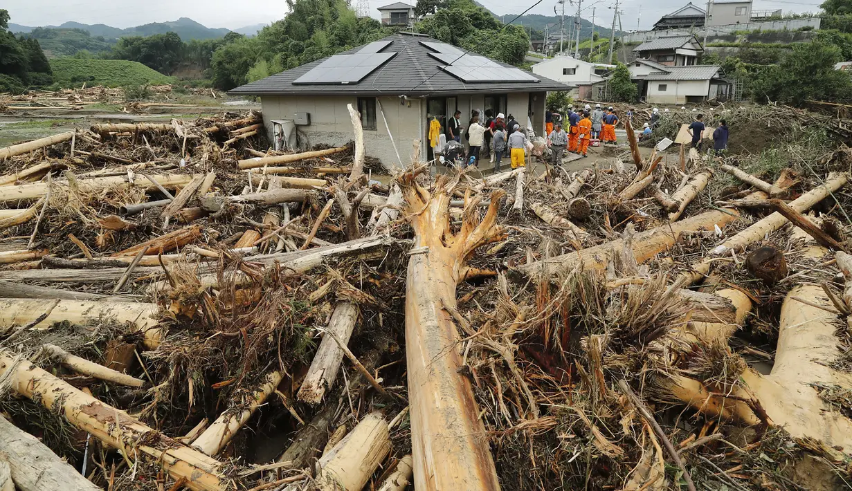 Petugas penyelamat dan penduduk memanfaatkan jeda hujan untuk membersihkan pohon-pohon, dan lumpur setinggi lutut yang memenuhi jalanan di Toho, prefektur Fukuoka, Jepang, Sabtu (8/7). (AFP PHOTO / JIJI PRESS)