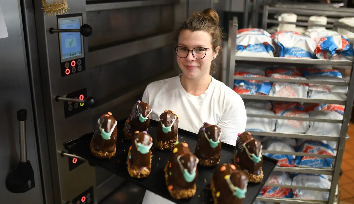 Pembuat roti Andrea Schulz menunjukkan nampan berisi kue cokelat Paskah berbentuk domba tradisional dengan masker di toko roti Schuerener Backparadies, Dortmund, Jerman, Rabu (8/4/2020). Pembuatan kue Paskah dengan masker bertepatan dengan pandemi virus corona COVID-19. (Ina FASSBENDER/AFP)