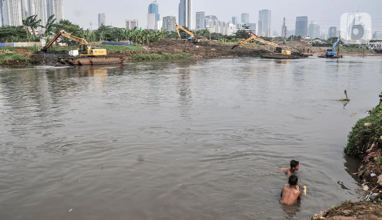 Anak-anak berenang dekat alat berat yang tengah mengerjakan pengerukan lumpur di Kali Ciliwung Segmen Kanal Banjir Barat (KBB), Tanah Abang, Kamis (30/9/2021). Pengerukan dilakukan untuk memperbesar daya tampung sekaligus mengantisipasi banjir pada musim hujan. (merdeka.com/Iqbal S. Nugroho)