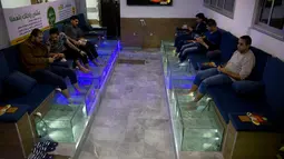 Warga Palestina merendam kaki mereka dalam akuarium berisi ikan di sebuah kafe di Kota Gaza, Palestina, Rabu (26/12/2018). Pedikur ikan tersebut dibanderol dengan harga 30 syikal atau sekitar 8 dolar AS per 30 menit. (AP Photo/Khalil Hamra)