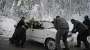 Orang-orang mendorong kendaraan yang terjebak salju di sepanjang jalan Bukit Murree, Pakistan, 9 Januari 2022. Sebanyak 22 wisatawan tewas saat sekitar 1.000 kendaraan terjebak salju tebal di Bukit Murree. (Aamir QURESHI/AFP)
