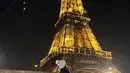 Berpose di depan menara Eiffel, Anya mengenakan pakaian serba hitam berupa coat, celana panjang, dan combat boots. (Instagram/anyageraldine).