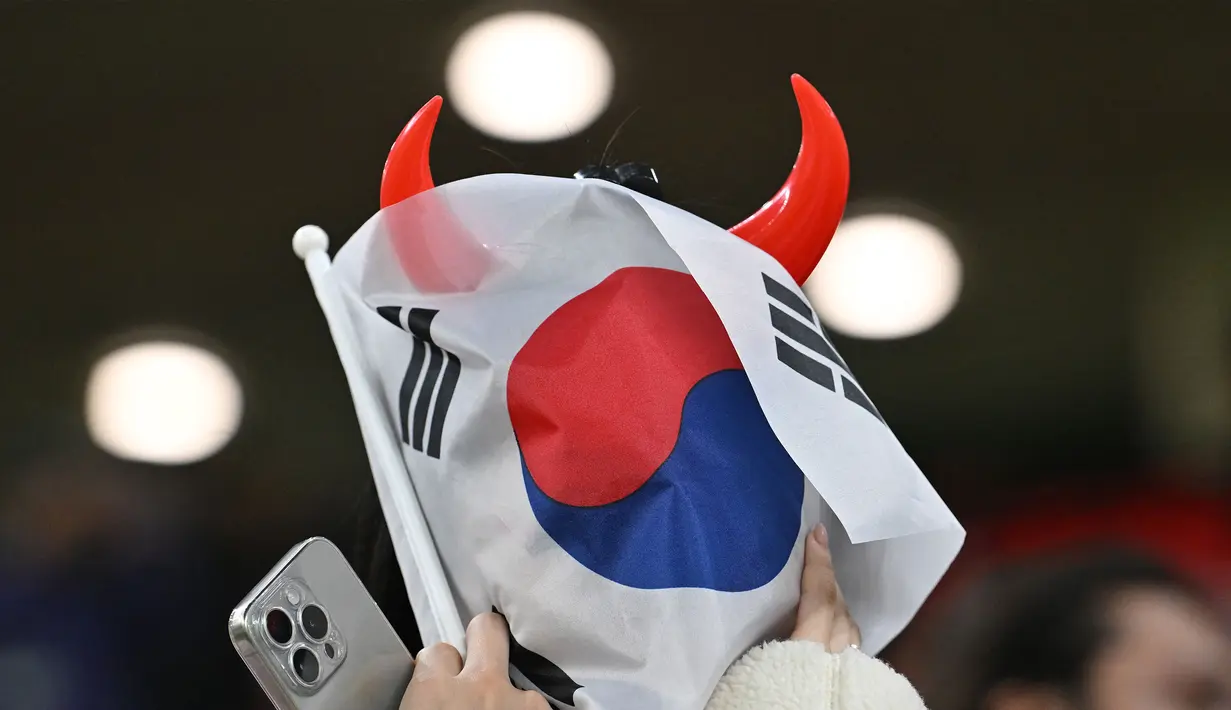 Seorang suporter Korea Selatan menutup muka menggunakan bendera negaranya setelah timnya kalah dari Yordania pada laga semifinal Piala Asia 2023 di Ahmad Bin Ali Stadium, Doha, Qatar, Selasa (06/02/2024). Korea Selatan kalah dengan skor 0-2. (AFP/Hector Retamal)