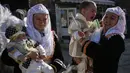 Wanita muslim Bulgaria menggendong putra mereka selama upacara sunat massal untuk anak laki-laki di Desa Ribnovo, 11 April 2021. Penduduk Desa Ribnovo adalah muslim berbahasa Bulgaria, kadang-kadang disebut sebagai "Pomaks" atau "orang yang menderita". (Nikolay DOYCHINOV/AFP)