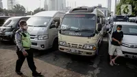 Polisi berjalan melewati kendaraan travel gelap yang disita jajaran Direktorat Lalu Lintas Polda Metro Jaya, Jakarta, Kamis (29/4/2021). Sebanyak 115 kendaraan travel gelap diamankan karena diduga kuat mengangkut pemudik di tengah masa pengetatan larangan mudik 2021. (Liputan6.com/Faizal Fanani)