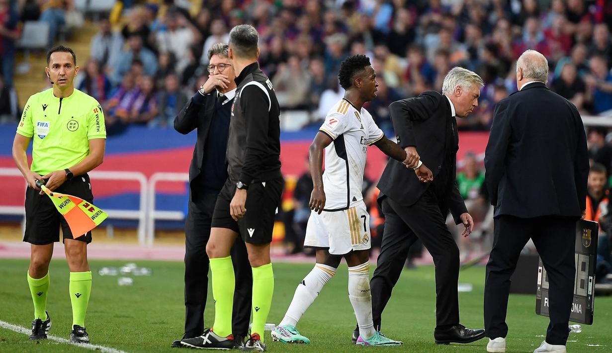 Pelatih Real Madrid, Carlo Ancelotti menarik tangan Vinicius Junior dan memaksanya untuk keluar dari lapangan saat pertandingan lanjutan Liga Spanyol 2023/2024 melawan Barcelona yang berlangsung di Estadi Olimpic Lluis Companys, Minggu (29/10/2023) dini hari WIB. (AFP/Josep Lago)