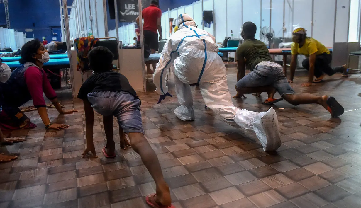 Seorang dokter yang mengenakan setelan Alat Pelindung Diri memberikan instruksi kepada pasien saat melakukan yoga di dalam bangsal di kompleks olahraga Commonwealth Games (CWG) Village yang sementara diubah menjadi pusat perawatan Covid-19 di New Delhi, India, Kamis (16/7/2020). (Money SHARMA / AFP)