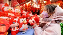Seorang anak memilih mainan menjelang Hari Tahun Baru di sebuah pasar di Qingdao, di provinsi Shandong timur China pada 25 Desember 2022. Warga China mulai berburu pernak-pernik Tahun Baru seperti lampion, kartu tahun baru, baju, dan hiasan rumah. (AFP/STR)