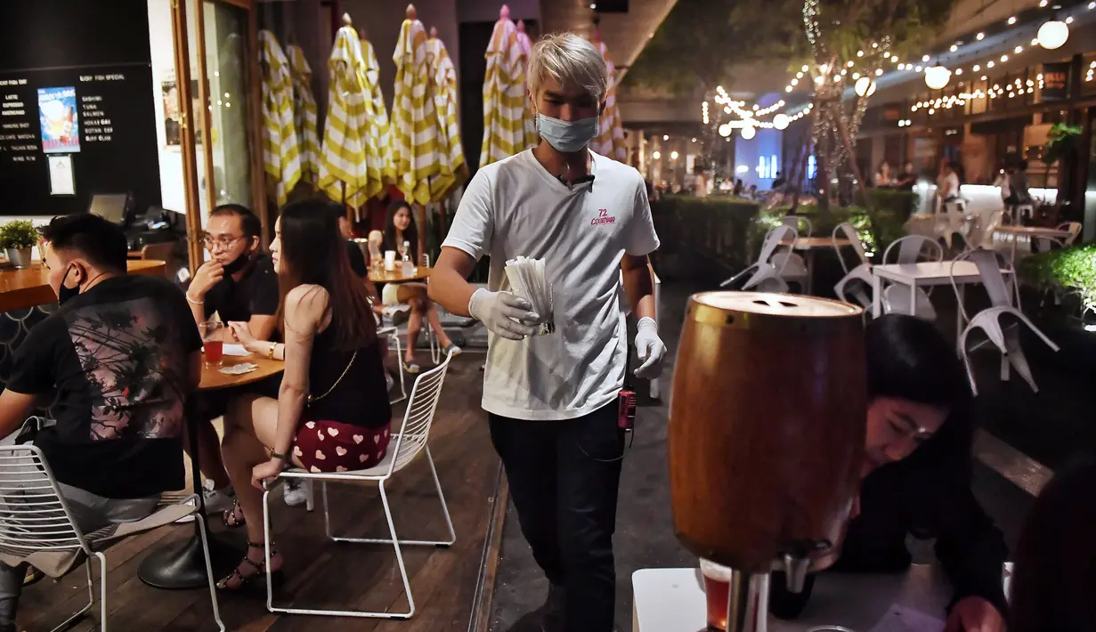 Pelayan melayani pelanggan di sebuah bar di Bangkok, Thailand, Rabu (1/7/2020). Mulai 1 Juli, bar di Bangkok kembali diizinkan buka setelah pengurangan pembatasan akibat COVID-19. (Lillian SUWANRUMPHA/AFP)
