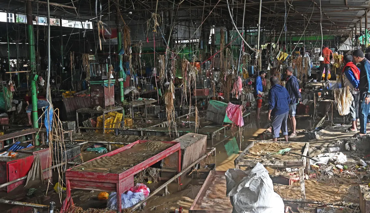 Para pedagang membersihkan lumpur dan puing-puing di sebuah pasar sayur di daerah yang terkena dampak banjir setelah hujan lebat di Kathmandu pada tanggal 29 September 2024. (PRAKASH MATHEMA/AFP)
