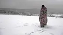 Seorang migran berjalan melewati salju dengan dibungkus selimut di kamp Lipa, barat daya Bosnia, dekat perbatasan dengan Kroasia, Sabtu (26/12/2020). Para imigran membungkus tubuh mereka dalam balutan selimut dan kantong tidur untuk melindungi diri dari serangan angin dingin. (AP Photo/Kemal Softic)