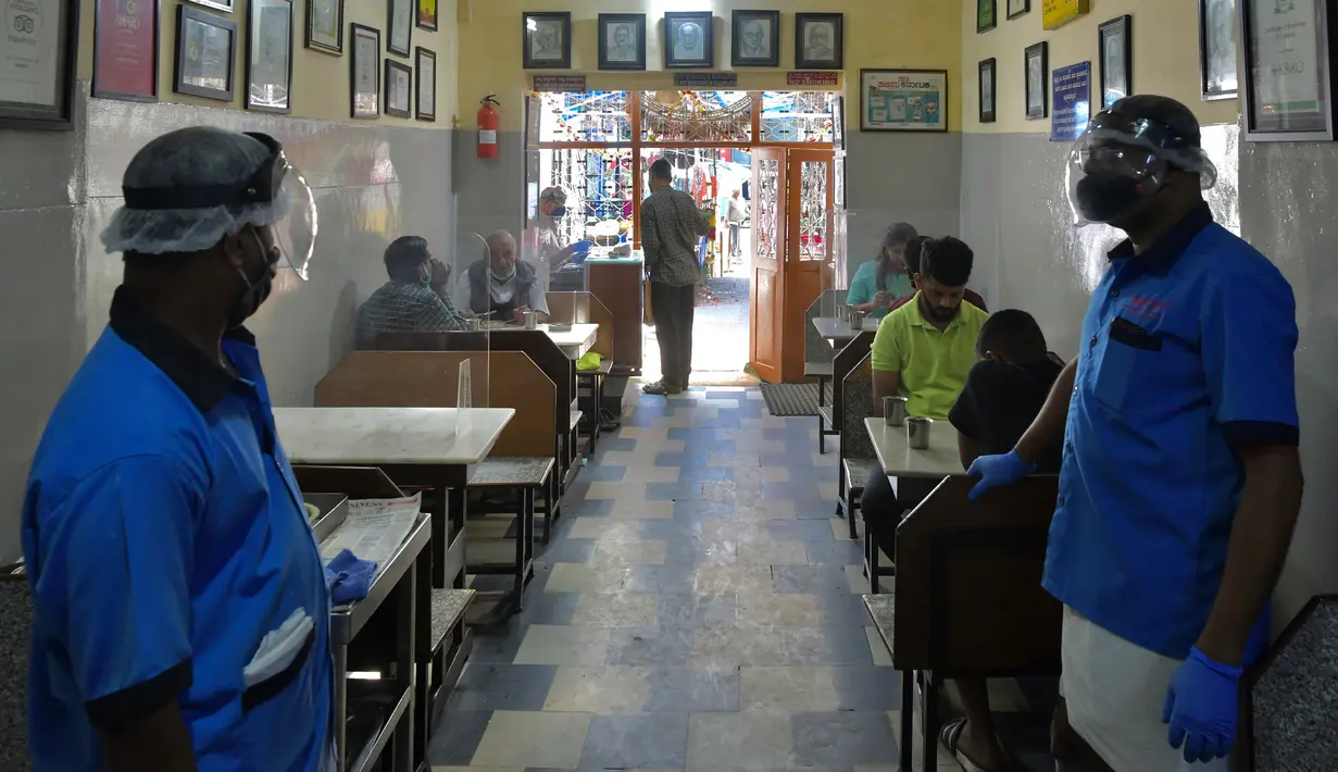Pramusaji mengenakan pelindung wajah dan masker di sebuah restoran yang dibuka kembali usai pelonggaran lockdown di Bangalore, India, Senin (8/6/2020). Untuk keamanan pelanggan, restoran-restoran menyiapkan panel transparan di meja makan sebagai pencegahan COVID-19. (Manjunath Kiran/AFP)