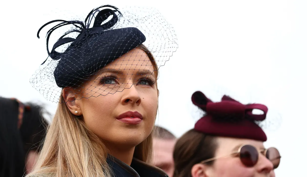 Dua wanita menunggu untuk menyaksikan dimulainya balapan pada hari pertama Festival Cheltenham di Cheltenham Racecourse, di Cheltenham, Inggris (15/3/2022). Festival empat hari berlangsung setiap tahun pada bulan Maret di Cheltenham Racecourse di Cheltenham, Gloucestershire. (AFP/Adrian Dennis)