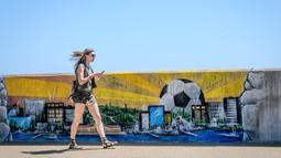 Seorang wanita melintas dekat mural seputar Fisht Olympic Stadium di Sochi, Rusia, (17/5/2018). Stadion tersebut akan menjadi saksi laga perdana Portugal melawan Spanyol. (AFP/Mladen Antonov)