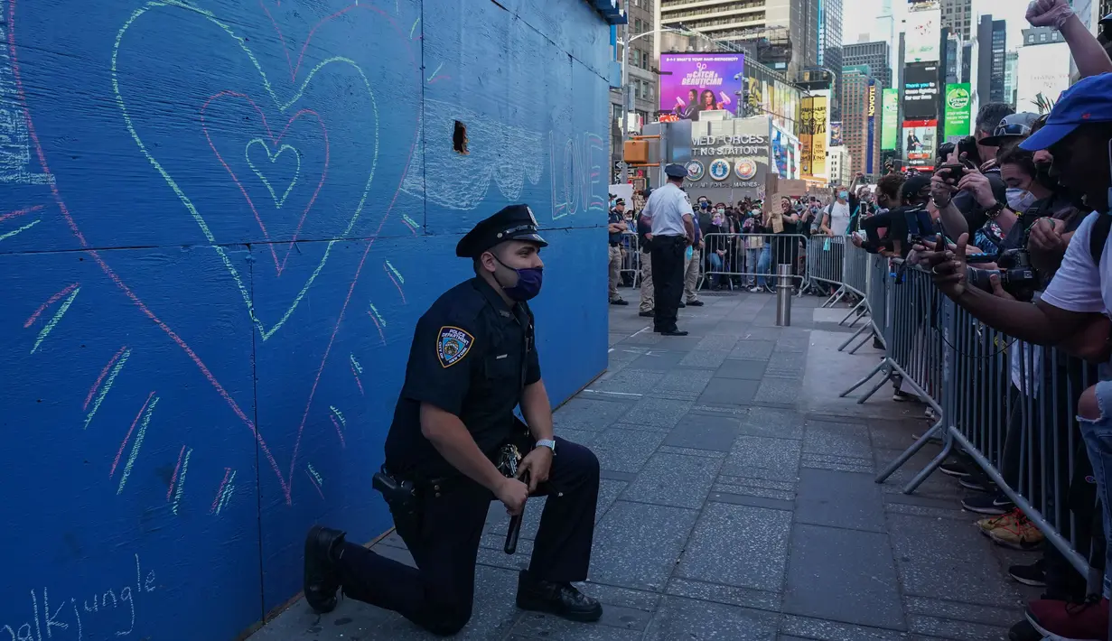 Seorang perwira polisi Kota New York berlutut saat pengunjuk rasa berdemonstrasi atas kematian George Floyd di Times Square, New York pada 31 Mei 2020. George Floyd, pria kulit hitam itu tewas tak bisa bernafas karena tercekik lutut polisi saat ditangkap pada (25/5/2020) lalu. (Bryan R. Smith / AFP)
