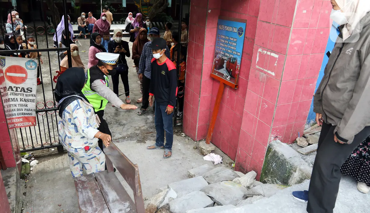 Polisi mengatur perlintasan jalan darurat yang dibuat pihak sekolah di SDN Pondok Cina 1, Depok, Jawa Barat, Rabu (9/11/2022). Pembangunan trotoar Jalan Margonda Raya yang tidak membuat jalan darurat untuk siswa tersebut menghalangi pintu masuk SDN Pondok Cina 1 serta membahayakan siswa. (Liputan6.com/Herman Zakharia)